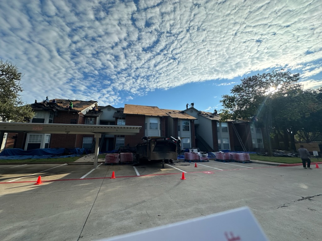 Multi-unit residential roofing project in progress in Dallas area, showing professional roofers working on apartment complex with materials and equipment staged