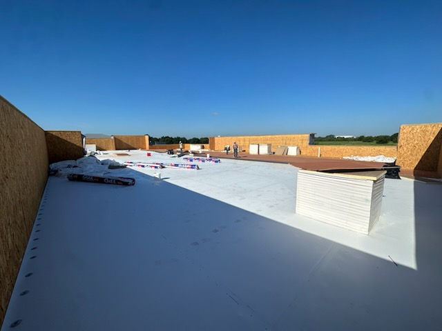 Commercial flat roof installation in Waxahachie TX showing white TPO membrane with stacked insulation boards